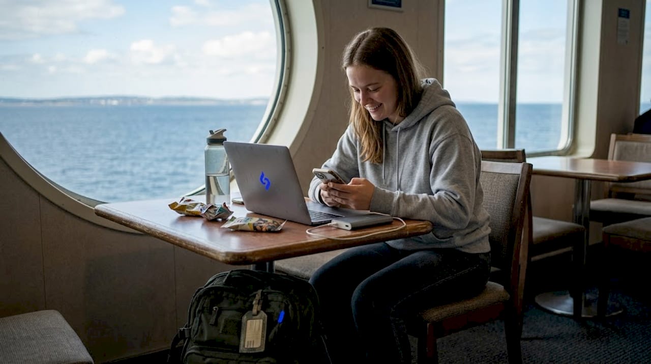Une femme profite de la traversée en ferry pour consulter son téléphone, tout en admirant la mer qui s’étend à perte de vue.