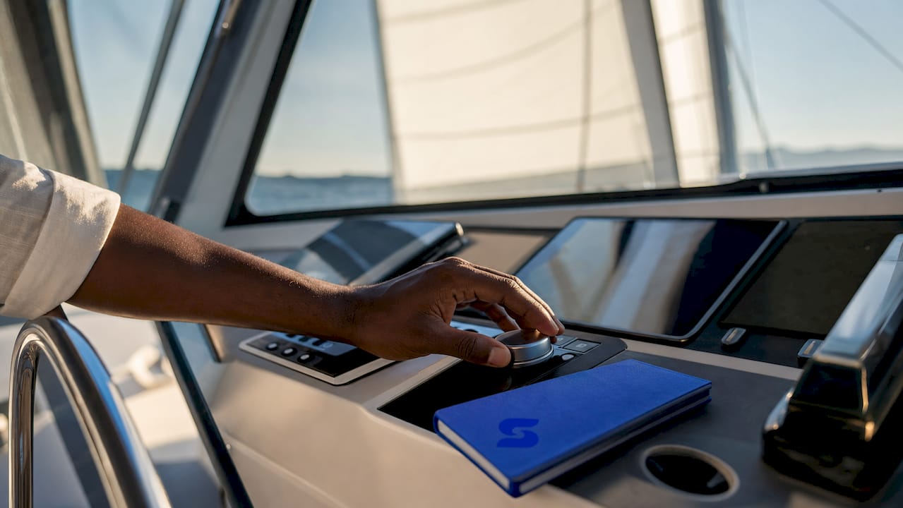Une main posée sur l’écran tactile commande l’interface numérique du navire.