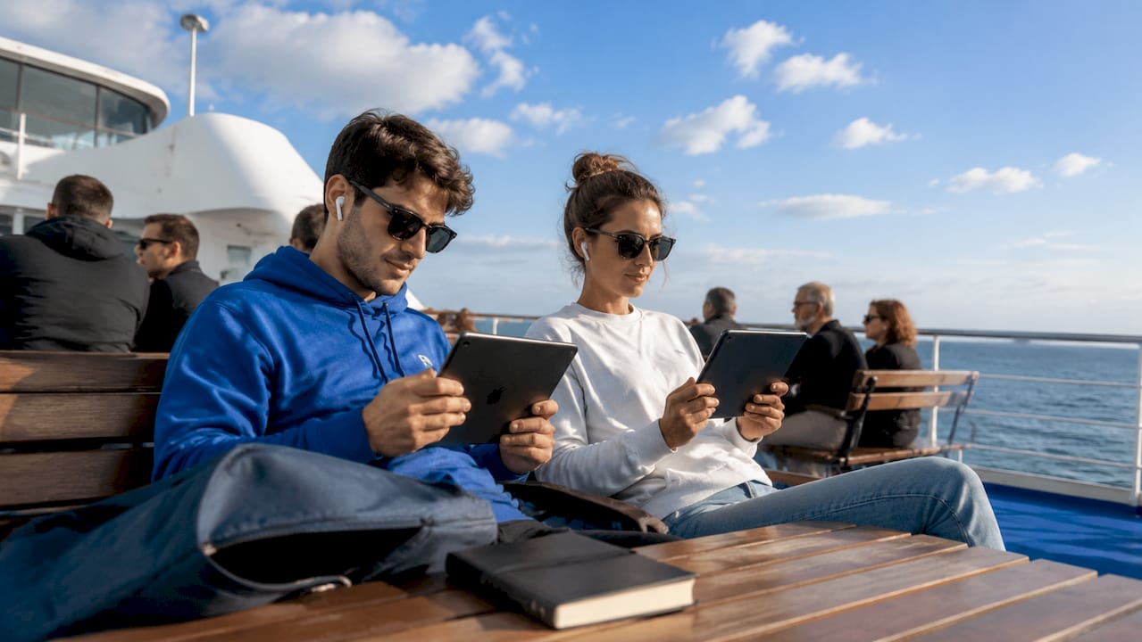 Sul traghetto, alcuni ragazzi si intrattengono ascoltando musica con le cuffie e smanettando sui tablet.