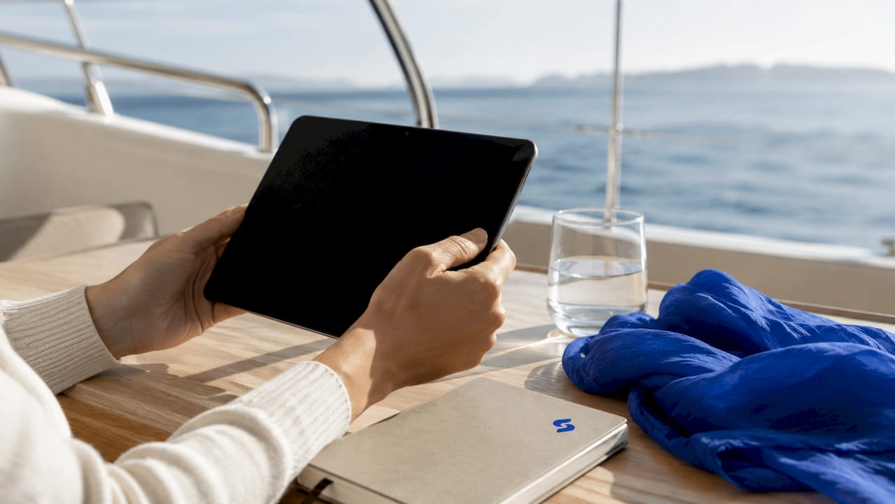 Des mains tiennent une tablette, posées sur le pont d’un ferry.